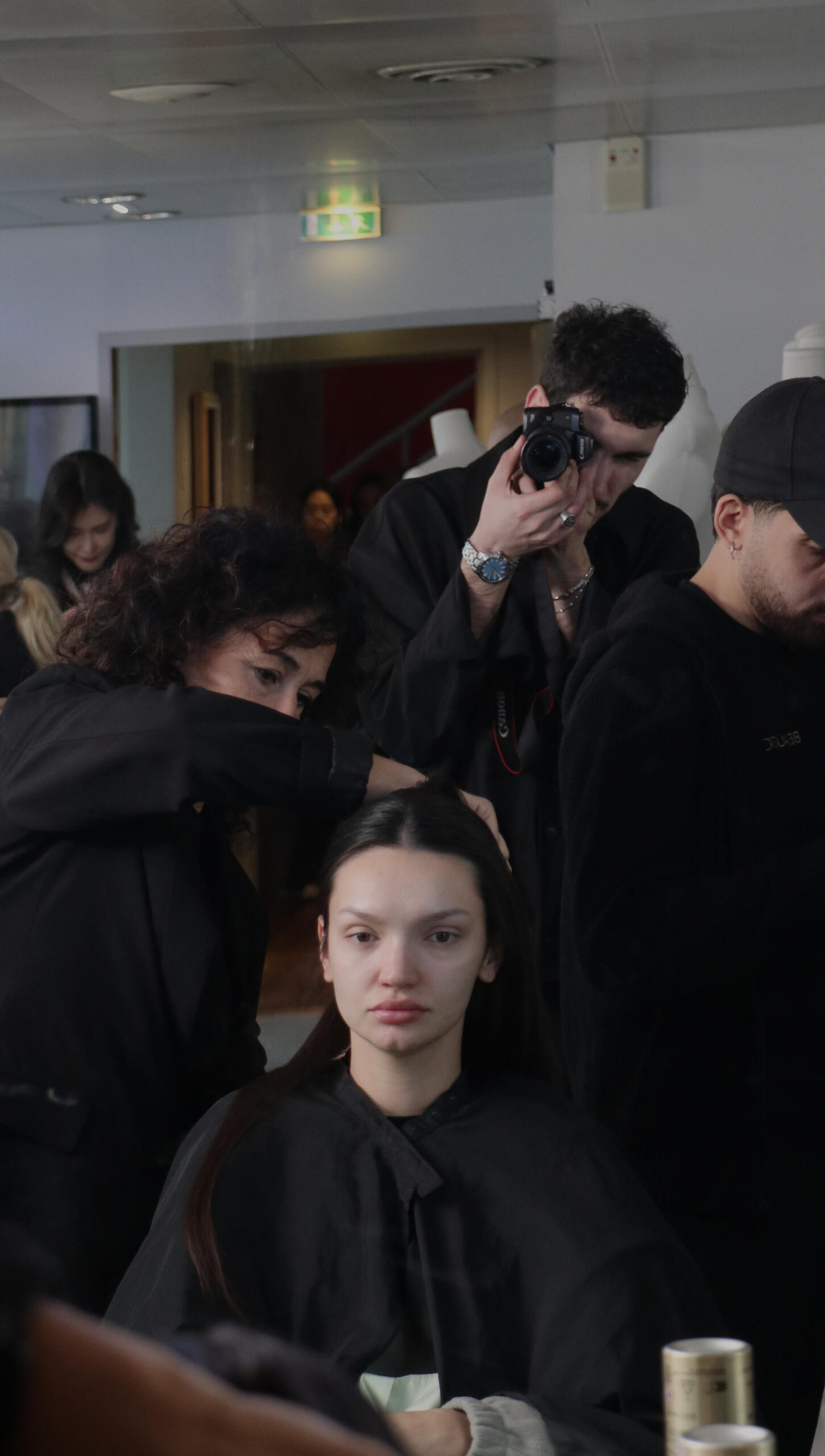Backstage: un fotografo scatta mentre l'hair stylist prepara la modella